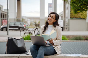 Portrait of confident smiling businesswoman using laptop computer holding notepad looking at camera working outdoors. Successful business 