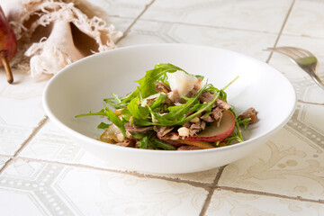 bowl with salad with arugula, duck, pear, nuts and parmesan on a light table