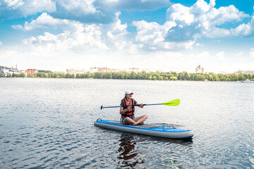 Charming smiling woman rides a sup paddle board around city lake