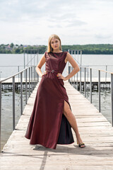 Beautiful girl in long fashionable dark red dress near pond in sity park