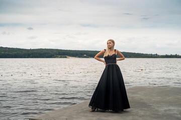 Fototapeta na wymiar beautiful blonde girl in a black elegant fashionable dress stand near lake