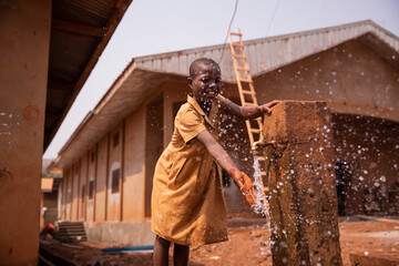 African schoolchild plays splashing water from the tap placed outside in the schoolyard