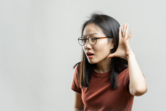 Portrait of a Korean girl on a gray background. Asian woman eavesdropping