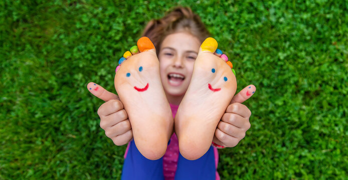 Feet of a child on the grass with a painted smile. Selection focus.