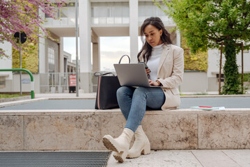 Pensive stylish businesswoman holding mobile phone using laptop computer working online on the...