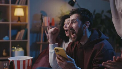 Happy surprised people emotionally enjoying success or good news, or mobile online bet bid game while sitting together at home and supporting favorite team. Sports betting concep.