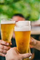 Close-up view of a three glass of beer in hand. Beer glasses clinking at outdoor bar or pub