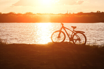 Fototapeta na wymiar Silhouette bicycle against background river and bright red sunset.