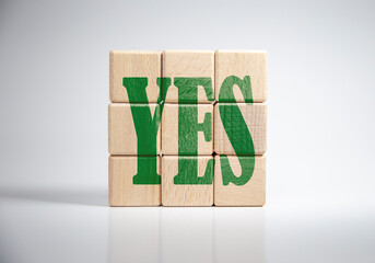 Lettering the word YES on a wooden block placed on a white background.