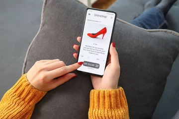 Foto op Plexiglas Closeup of woman doing online shopping on smartphone at home. Rear view of woman hand touching screen while selecting shoes on e commerce portal. Lady use e-commerce web shop to buy high heels. © Boris