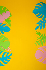 Fototapeta na wymiar colorful jungle leaves on the left and right of the yellow background, in the middle copy space, creative exotic design, flat lay, jungle party