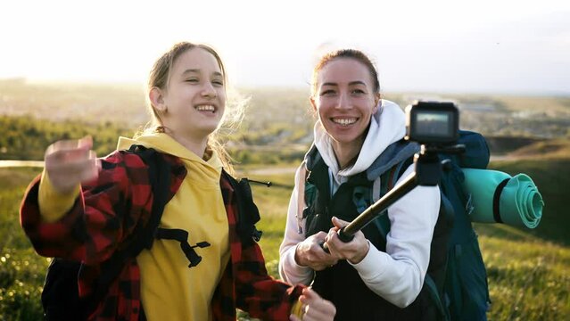 Mom and daughter in nature shoot video blog on camera a selfie stick about tourist trip on mountain. Family walk in outdoor at weekend. Healthy lifestyle. Happy girls at good emotions smile and laugh