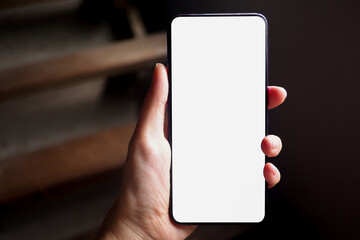 Mockup picture of business woman’s hands holding smart phone with white blank screen in modern place.