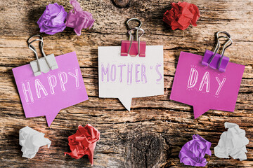 happy mother's day written in English on scraps of paper in the shape of bubbles, rustic wooden table