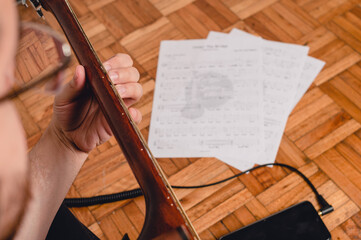 top view man sitting on the floor practicing guitar with sheet music on the floor