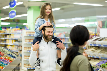 A young family with a little girl choose candy and chocolate in a large store, supermarket.