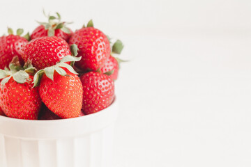 Red strawberries in a white bowl on a white background. Sweet breakfast with spring strawberry. Copy space.