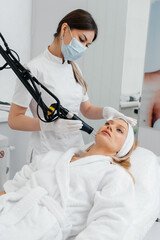 A young girl gets a charcoal peeling for the skin of the face in a beauty salon. Laser pulses cleanse the skin. Hardware cosmetology. The process of photothermolysis, warming the skin.