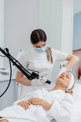 Obraz premium A young girl gets a carbon peeling for the skin of the neck in a beauty salon. Laser pulses cleanse the skin. Hardware cosmetology. The process of photothermolysis, warming the skin.