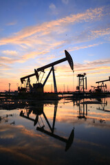Obraz premium in the evening, oil pumps are running, The oil pump and the beautiful sunset reflected in the water, the silhouette of the beam pumping unit in the evening.