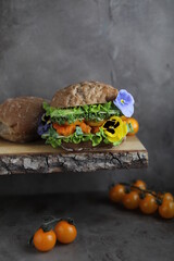 Appetizing sandwich with fish fingers, cucumber, yellow cherry tomato, avocado, microgreens, cheese and edible viola flowers. Fresh light snack.