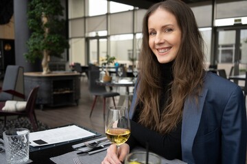 Beautiful happy young woman smiling, tasting red wine, holding wineglass, sitting at the dining table in a restaurant.
