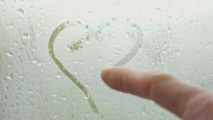 Man draws heart on fogged window with finger. Rain outside leaves drops on misted glass. Cute heart shape come out from male finger, sunlight - Powered by Adobe