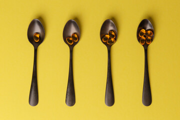 The concept of a healthy lifestyle. Fish oil - useful vitamin supplements on black metal spoons on a yellow background. Close-up, top view. Medical preparations. Natural additives.