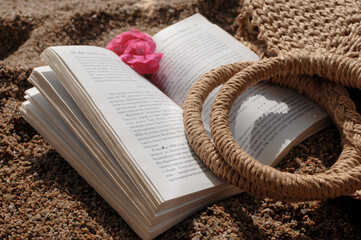 Close up of beach accessories: straw knitted bag and a book on a sandy beach