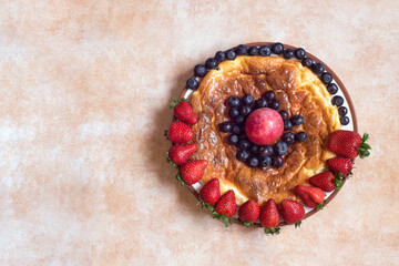 Overhead view of a Round plate with delicious homemade cheesecake surrounded by strawberries with red plum and blueberries on a pastel-colored studio background and copy space.