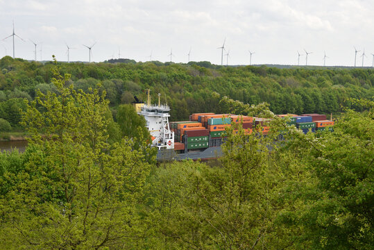 Containerschiff fährt auf dem Nord-Ostsee-Kanal durch Laubwald 