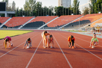 A large group of girls, are taught by a coach at the start before running at the stadium during sunset. A healthy lifestyle.