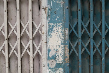 Close-up of old metal curtains with cross and rust; old sliding metal door, closed and abandoned storefront, metallic gate background