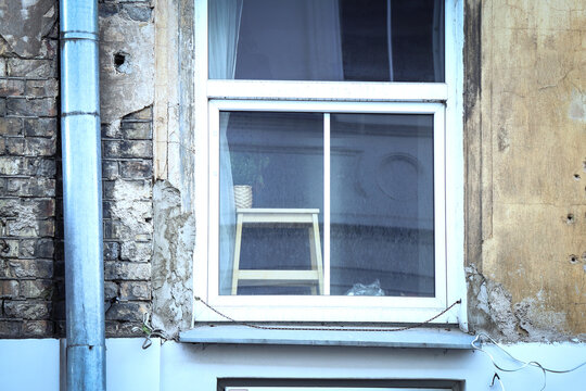 Window with modern plastic frame with old wooden stool visible behind the glass in old building with stainless steel water drain pipe