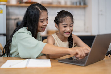 Mother and asian kid little girl online learning on laptop computer making homework studying knowledge with online education e-learning system. children video conference with teacher tutor at home