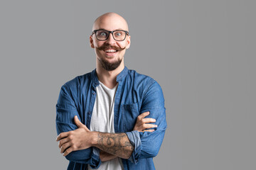 Studio shot of young happy man smiling with wide open eyes while wearing eyeglasses with arms crossed - obrazy, fototapety, plakaty