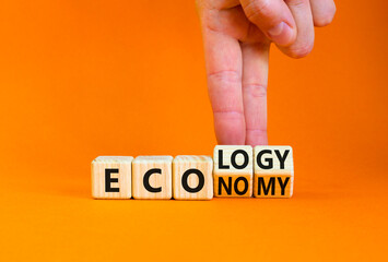 Ecology or economy symbol. Businessman turns wooden cubes and changes the concept word Economy to Ecology. Beautiful orange table orange background. Business ecology or economy concept. Copy space.