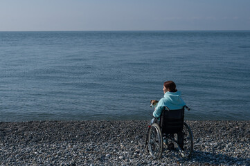 Caucasian woman in a wheelchair cuddling with a dog near the sea. 