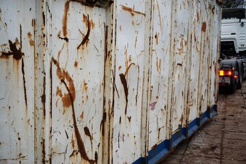 Alter weißer Müllcontainer mit Rostablagerungen wird von Lastkraftfahrzeug gezogen 
