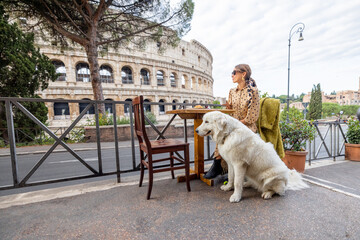 Woman sitting with her dog at outdoor cafe near coliseum, the most famous landmark in Rome. Concept...