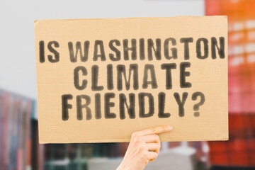 The question " Is Washington climate-friendly? " is on a banner in men's hands with blurred background. Support. Team. Activist. Urban. Sunset. Carbon. Ecology. Energy. New. Clean. Warming. Waste