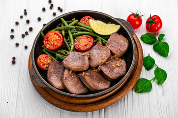 Fried beef tongue with green beans and tomatoes in a pan.