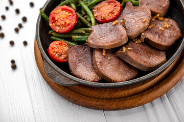 Fried beef tongue with green beans and tomatoes in a pan.