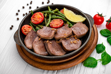 Fried beef tongue with green beans and tomatoes in a pan.