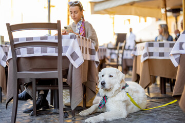 Woman sitting with her dog at traditional italian cafe outdoor. Concept of italian lifestyle and travel. Pet friendly cafe