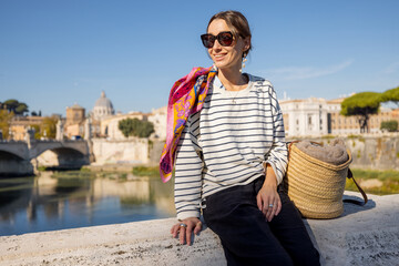 Woman enjoying beautiful view of Rome city and Vatican standing on the bridge on a sunny autumn day. Elegant woman wearing stripped blouse and shawl in hair. Concept of italian lifestyle and travel