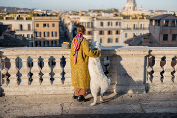 Woman enjoys beautiful cityscape of old Rome city, standing back with her dog on the top of Spanish...