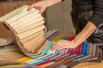 Fabric swatches in different colors are stacked for selection. A woman chooses upholstery colors...