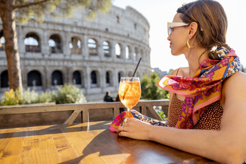 Woman drinking Spritz Aperol at outdoor cafe near Coliseum, the most famous landmark in Rome....