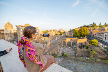 Fototapeta premium Woman enjoying view on the Roman Forum, ruins at the center of Rome on a sunset. Concept of traveling famous landmarks in Italy. Caucasian woman wearing colorful shawl in hair and sunglasses